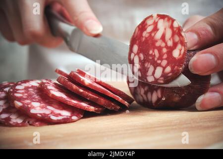 Das Messer schneidet die geräucherte Wurst in Stücke Stockfoto