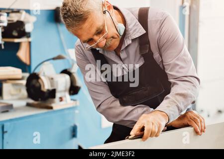 Porträt eines älteren Zimmermanns oder Zimmermanns, der mit Holzbrettern in einer Tischlerwerkstatt arbeitet. Stockfoto