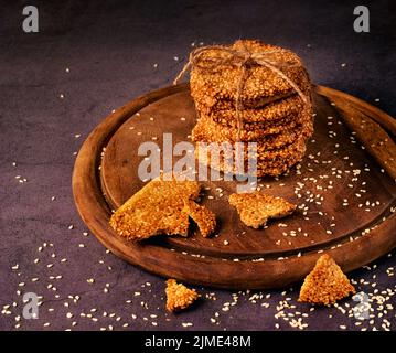 Foto eine Sesamkekse, die mit einem Seil auf einem Holzbrett mit Sesamsamen im Hintergrund gebunden ist Stockfoto