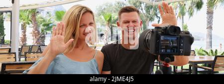 Glückliches Paar, das auf einem Stativ in einem Café auf die Kamera winkt Stockfoto