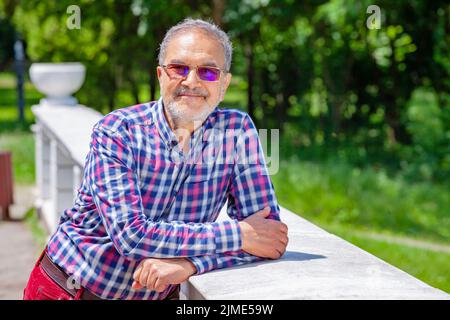 Entspannter Rentner mit legerer Kleidung und Brille im Park lächelnd Stockfoto