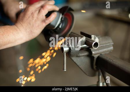 Ein Mann arbeitet an einem Teil in der Garage.Metallschleifen. Stahlbearbeitung mit Elektrowerkzeugen. Stockfoto