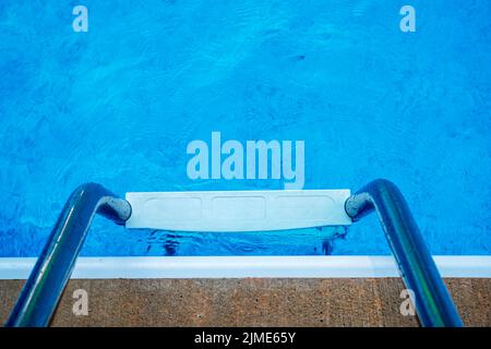 Blick auf die Leiter des Schwimmbads und das saubere, einladende blaue Wasser Stockfoto