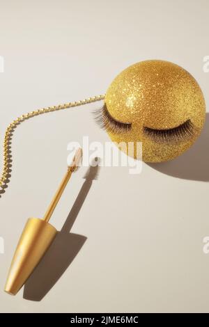 Mascara und ein goldener Weihnachtsball mit falschen Wimpern. Das Konzept der festlichen Make-up für Frauen. Stockfoto