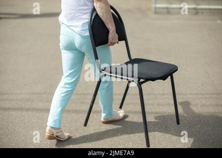 Das Mädchen trägt Stühle die Straße hinunter. Schwarzer Stuhl in der Hand des Mädchens. Stockfoto