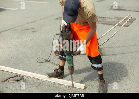 Er entfernt den Asphalt mit einem Presshammer. Entfernen der Asphaltschicht von der Straße. Stockfoto