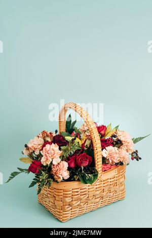 Ein weiden Strauß von Sommerblumen in einem Korbkorb steht auf einem zarten blauen Hintergrund. Stockfoto