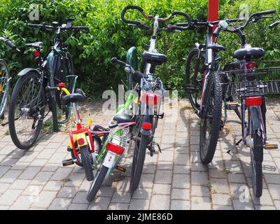 Eine Nahaufnahme von verschlossenen Familienfahrrädern, die vor Büschen in einem Park, Egelsbach, geparkt wurden Stockfoto