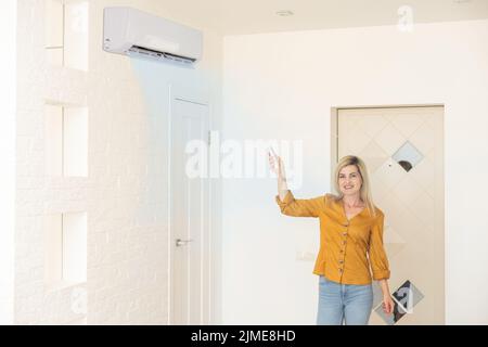 Frau mit Fernbedienung, die auf die Klimaanlage gerichtet ist Stockfoto