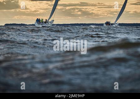 Wettbewerb von zwei Segelbooten am Horizont im Meer bei Sonnenuntergang, der erstaunliche Sturmhimmel in verschiedenen Farben, Rennen, große Wellen, Segel r Stockfoto