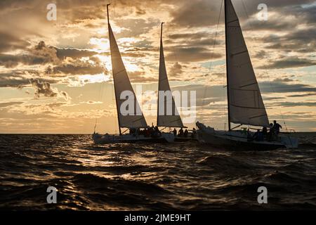 Wettbewerb von drei Segelbooten am Horizont im Meer bei Sonnenuntergang, der erstaunliche Sturmhimmel in verschiedenen Farben, Rennen, große Wellen, Segeln