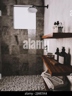 Badezimmer Holzregale mit Badeutensilien und Kosmetik im modernen grauen Badezimmer mit Dusche und Kieselsteinen auf dem Boden, modern Stockfoto