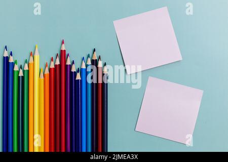 Buntstifte und ein Notenblatt liegen auf blauem Hintergrund. Draufsicht. Hintergrund To-do-Liste zurück in die Schule. Stockfoto