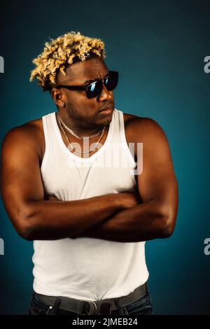 Ein schwül getragener Kerl mit modischer Frisur mit Zöpfen hält seine Hände auf der Brust und schaut weg. Stockfoto