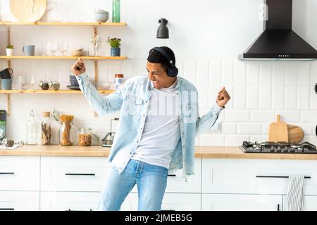 Glücklich unbeschwerte Freiheit junger Mann in Kopfhörern, der allein in der Küche nach Hause tanzt und Spaß hat Stockfoto