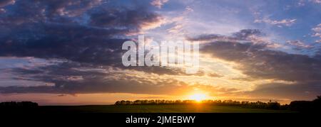 Panorama von orangefarbenem Sonnenuntergang bei Sonnenuntergang mit violetten Wolken am Horizont. Hintergrund verwischen. Stockfoto