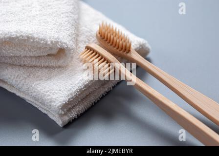 Zwei Zahnbürsten aus Holz und weiße Handtücher auf grauem Hintergrund Stockfoto