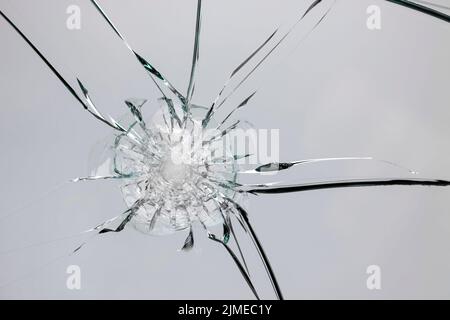 Risse auf zerbrochenem Glas durch Aufprall, weißer Rispenbrunnen auf dem Fenster. Stockfoto