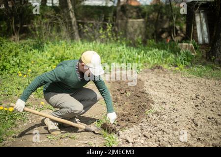 Kerl gräbt Erde mit Schaufel. Graben Boden für die Pflanzung. Arbeiten im Garten. Leben auf dem Land. Mann arbeitet. Stockfoto