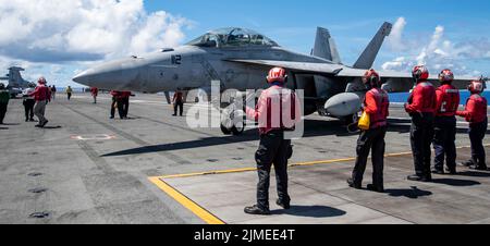 Philippinische See. 4. August 2022. Matrosen bereiten sich darauf vor, die Waffe auf einer F/A-18F Super Hornet zu entwaffnen, die an den 'Diamondbacks' des Strike Fighter Squadron (VFA) 102 auf dem Flugdeck des einzigen vorwärts eingesetzten Flugzeugträgers der US Navy USS Ronald Reagan (CVN 76) in der philippinischen See befestigt ist. Die Diamondbacks führen Luftangriff- und Streikkräfte-Escort-Missionen sowie Schiffe, Kampfgruppen und Geheimdiensteintreibereinsätze durch. Ronald Reagan, das Flaggschiff der Carrier Strike Group 5, stellt eine kampfbereite Truppe zur Verfügung, die die USA schützt und verteidigt, und unterstützt Allianzen, Partnerin Stockfoto