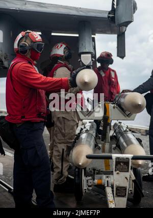 Philippinische See. 4. August 2022. Matrosen bereiten sich darauf vor, die Kampftruppe an eine F/A-18E Super Hornet zu übertragen, die an den 'Dambustern' des Strike Fighter Squadron (VFA) 195 auf dem Flugdeck des einzigen vorwärts eingesetzten Flugzeugträgers der US Navy USS Ronald Reagan (CVN 76) in der philippinischen See befestigt ist. Die Dambusters erhielten ihren Spitznamen am 1. Mai 1951, als die Skyraiders der Staffel den stark verteidigten und strategisch platzierten Hwacheon-Staudamm in Nordkorea mit Lufttorpedonen durch präzise Niederlagen zerstörten. Ronald Reagan, das Flaggschiff der Carrier Strike Group 5, liefert eine kampfbereite Fo Stockfoto