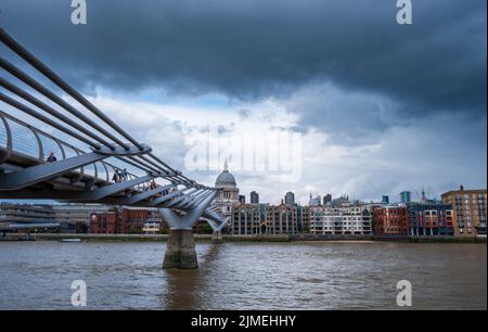 Blick auf die Millennium-Fußgängerbrücke, die in Richtung St. Paul's Cathedral führt, beleuchtet durch die Öffnung eines stürmischen Himmels. Stockfoto