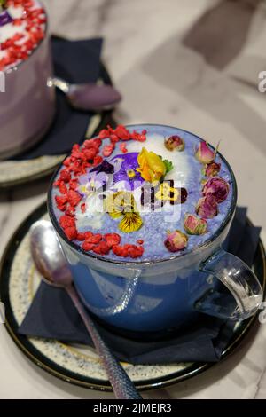 Tassen aus blauem Matcha, verziert mit essbaren Blumen, Rosenblättern und Glitzer Stockfoto