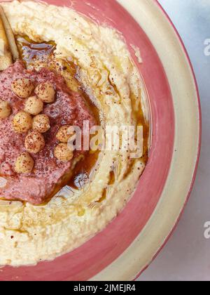 Hummus, arabischer Kichererbsen-Dip, mit Gewürzen auf einem rosa Cremeteller. Abstrakte Erfassung in der Draufsicht. Speicherplatz kopieren Stockfoto