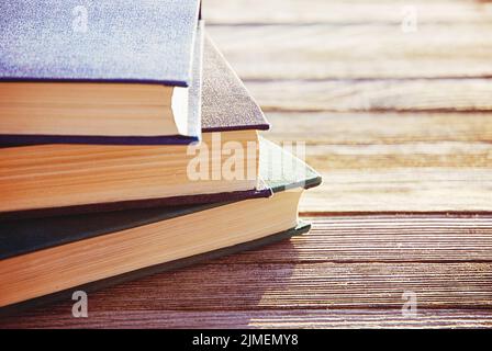 Stapel von drei alten Büchern in Hintergrundbeleuchtung auf Holztisch Stockfoto