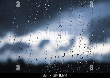 Regentropfen auf der Fensterscheibe. Schwarzer, grauer, weißer Farbverlauf auf verschwommenem Hintergrund. Wolkiges, regnerisches Wetter vor dem Fenster. Kühlung Stockfoto