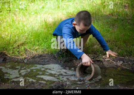 Das Kind hält einen verschmutzten Gegenstand. Kleiner Junge spielt mit Betonring. Kind hat etwas gefunden. Baby Abenteuer im Sommer. Stockfoto