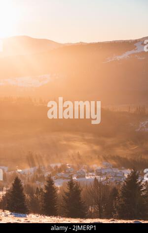Orangefarbenes Licht der Morgensonne strömt durch die Fichten in einem polnischen Dorf. Polnischer Teil der Beskiden im Morgengrauen. Stockfoto