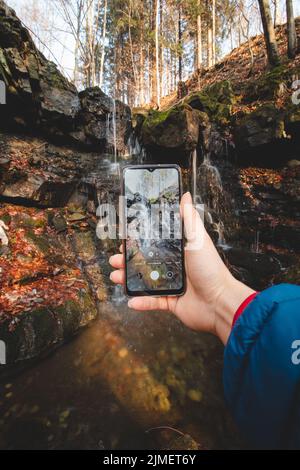 Tourist fotografiert den Tosanovsky Wasserfall auf seinem Handy für seine sozialen Netzwerke und für seine Erinnerungen. Beskiden, Tschechische republik, c Stockfoto