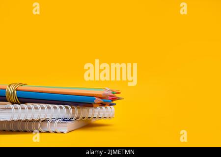 Buntstifte auf einem Stapel Notizbücher auf gelbem Hintergrund mit Platz für Text Stockfoto