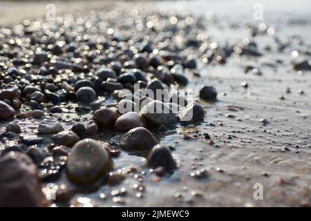 Kieselsteine am Strand der polnischen Ostseeküste bei Kolobrzeg bei Sonnenuntergang im Hintergrund Stockfoto