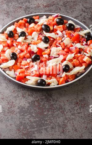 Katalanischer Kabeljau-Salat, auch bekannt als esqueixada, mit Kabeljau, Tomatenzwiebeln und Oliven-Nahaufnahme auf einem Teller auf dem Tisch. Vertikal Stockfoto