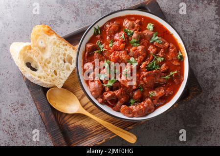 Brasilianisches portugiesisches Essen Moelas Guisadas geschmorte Hähnchenmagen in würziger Tomatensauce in einer Schüssel auf einem Holztablett auf dem Tisch. Horizontal t Stockfoto