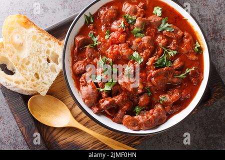 Moelas Guisadas schmorte langsam Hühnermagen in Tomatensauce aus der Nähe in einer Schüssel auf einem Holztablett auf dem Tisch. Horizontale Ansicht von oben Stockfoto