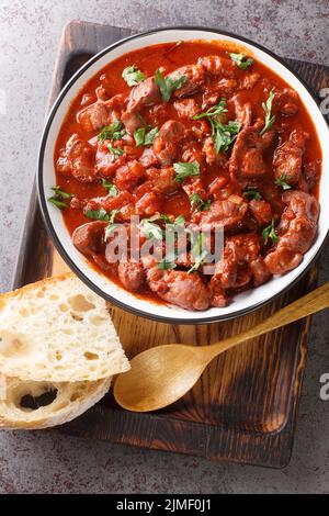 Moelas Guisadas Portugiesisches Huhn Gizzard Eintopf mit Tomate und Rotwein aus nächster Nähe in einer Schüssel auf dem Holztablett. Vertikale Ansicht von oben Stockfoto