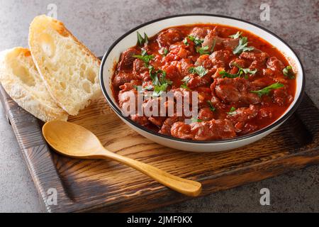 Brasilianisches portugiesisches Essen Moelas Guisadas Schmorhähnchen in würziger Tomatensauce in einer Schüssel auf einem Holztablett auf dem Tisch. Horizontal Stockfoto