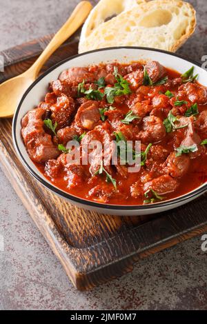 Moelas Guisadas Portugiesisches Huhn Gizzard Eintopf mit Tomaten und Rotwein aus nächster Nähe in einer Schüssel auf dem Holztablett. Vertikal Stockfoto