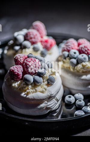 Köstliche Mini-pavlova-Süßspeisen mit gefrorenen, frostigen Beeren und Mascarpone-Schlagkäse Stockfoto