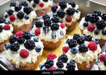 Hausgemachte Cupcakes verzierten weiße Creme und Waldbeeren, leckere und frische Süßigkeiten Stockfoto