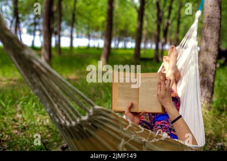 Frauen legen und lesen ein Buch auf der Hängematte im Wald Stockfoto