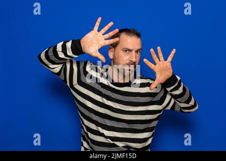 Ernsthafter und konzentrierter Mann mit den Händen vor seinem Gesicht als Zeichen der Verteidigung und des Schutzes. Stockfoto