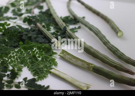 Trommelstock oder Moringa. Es ist ein Superfood mit viel Nährwert. Aufnahme zusammen mit Moringa-Blättern auf weißem Hintergrund. Stockfoto