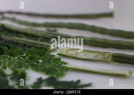 Trommelstock oder Moringa. Es ist ein Superfood mit viel Nährwert. Aufnahme zusammen mit Moringa-Blättern auf weißem Hintergrund. Stockfoto