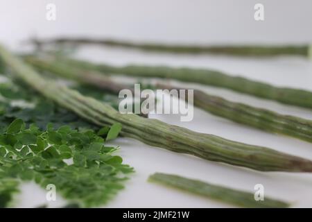 Trommelstock oder Moringa. Es ist ein Superfood mit viel Nährwert. Aufnahme zusammen mit Moringa-Blättern auf weißem Hintergrund. Stockfoto