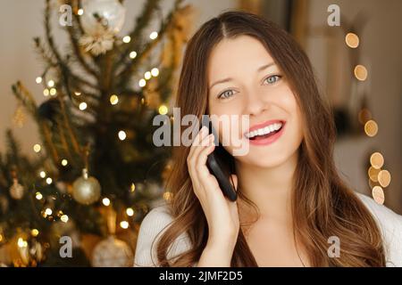 Weihnachts-Telefongespräch und Weihnachtsgruß-Konzept. Fröhliche lächelnde Frau, die am Weihnachtstag auf dem Handy spricht Stockfoto