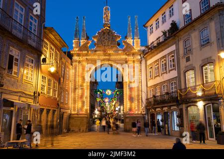 Braga, PORTUGAL - 25. Juni 2022: Menschen rund um den beleuchteten Arco da Porta Nova in Braga bei Dämmerung/blauer Stunde. Stockfoto